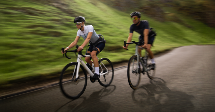 Two cyclists riding on a road with greenery in the background